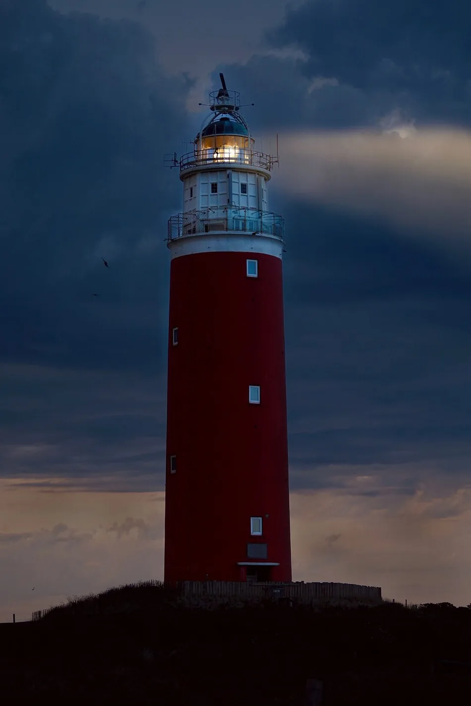 Roter Leuchtturm mit brennendem Licht vor nächtlichem Himmel